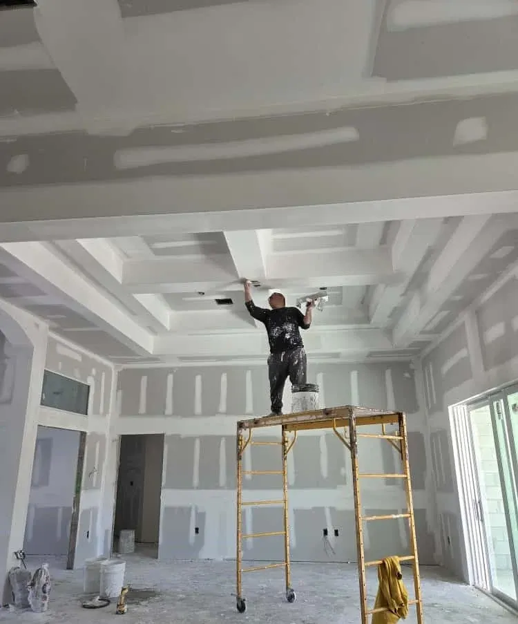 Drywall finisher working on a coffered ceiling from a rolling scaffold