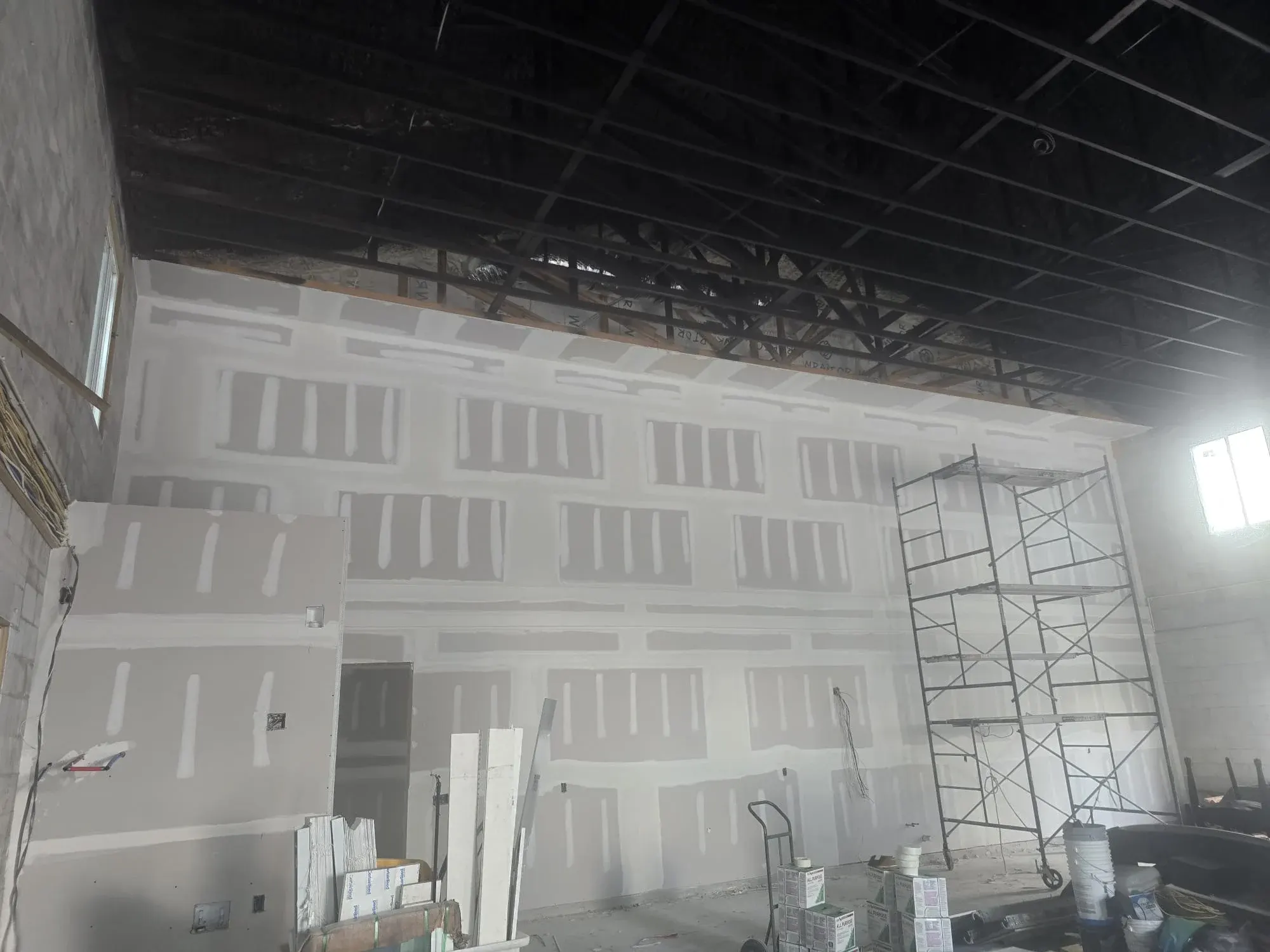 Taped and first-coated drywall walls beside a rolling scaffold, drywall finishing in Lehigh Acres